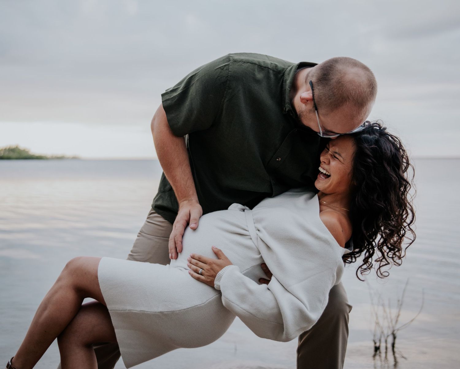 A couple shares heartfelt laughs and embraces on a cloudy beach.