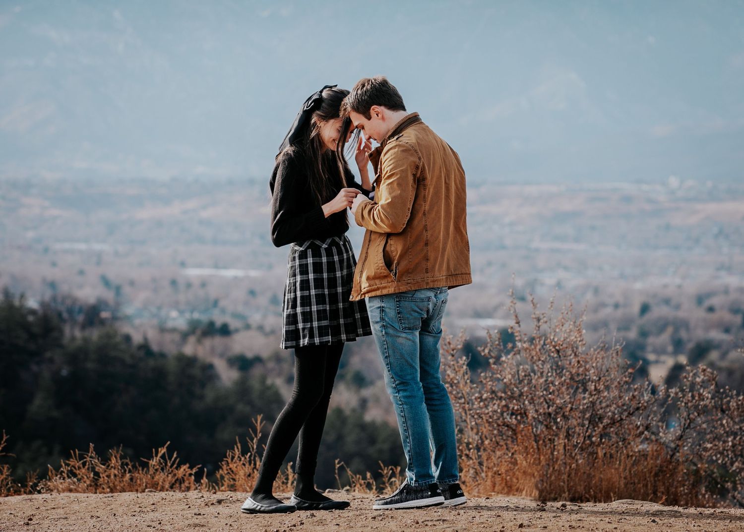 Newly engaged couple shares intimate moment with mountain vista behind them.