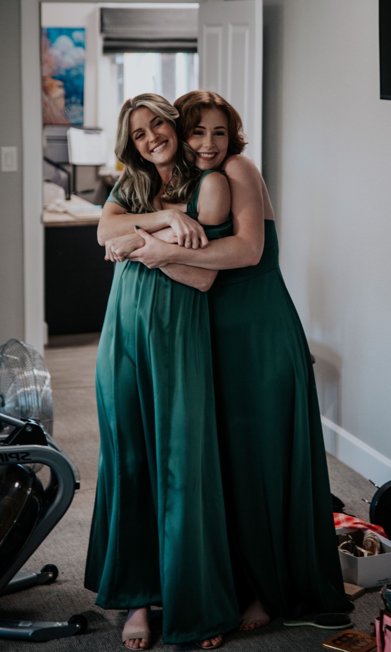 Two women in emerald green formal dresses embracing and smiling.