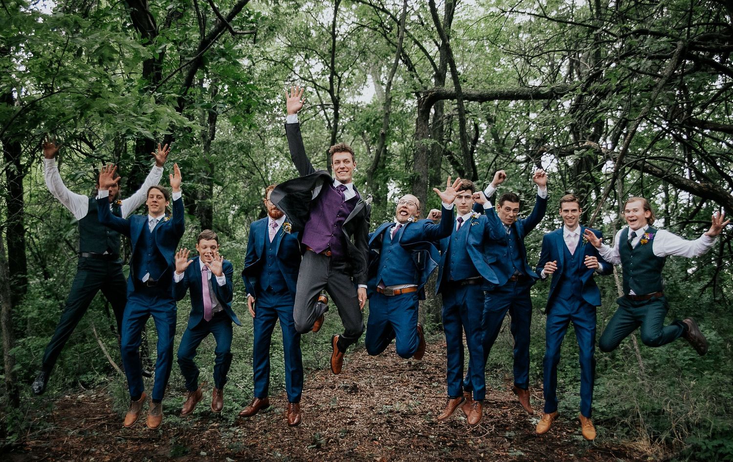 Wedding party group photo taken in a lush green forest setting.