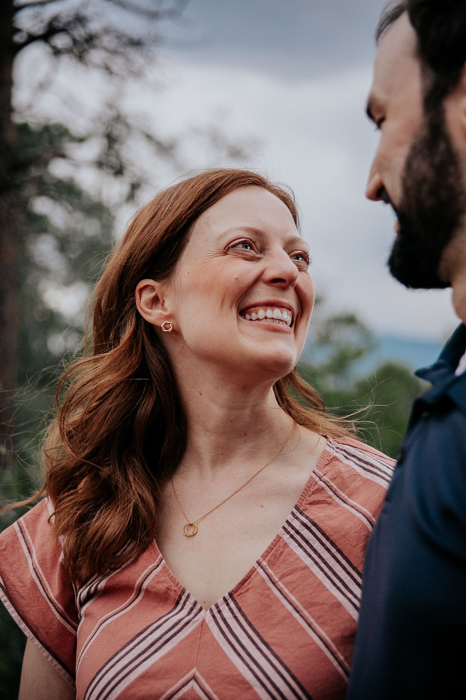 A couple shares intimate moments and laughter outdoors while wearing a striped dress and dark shirt.