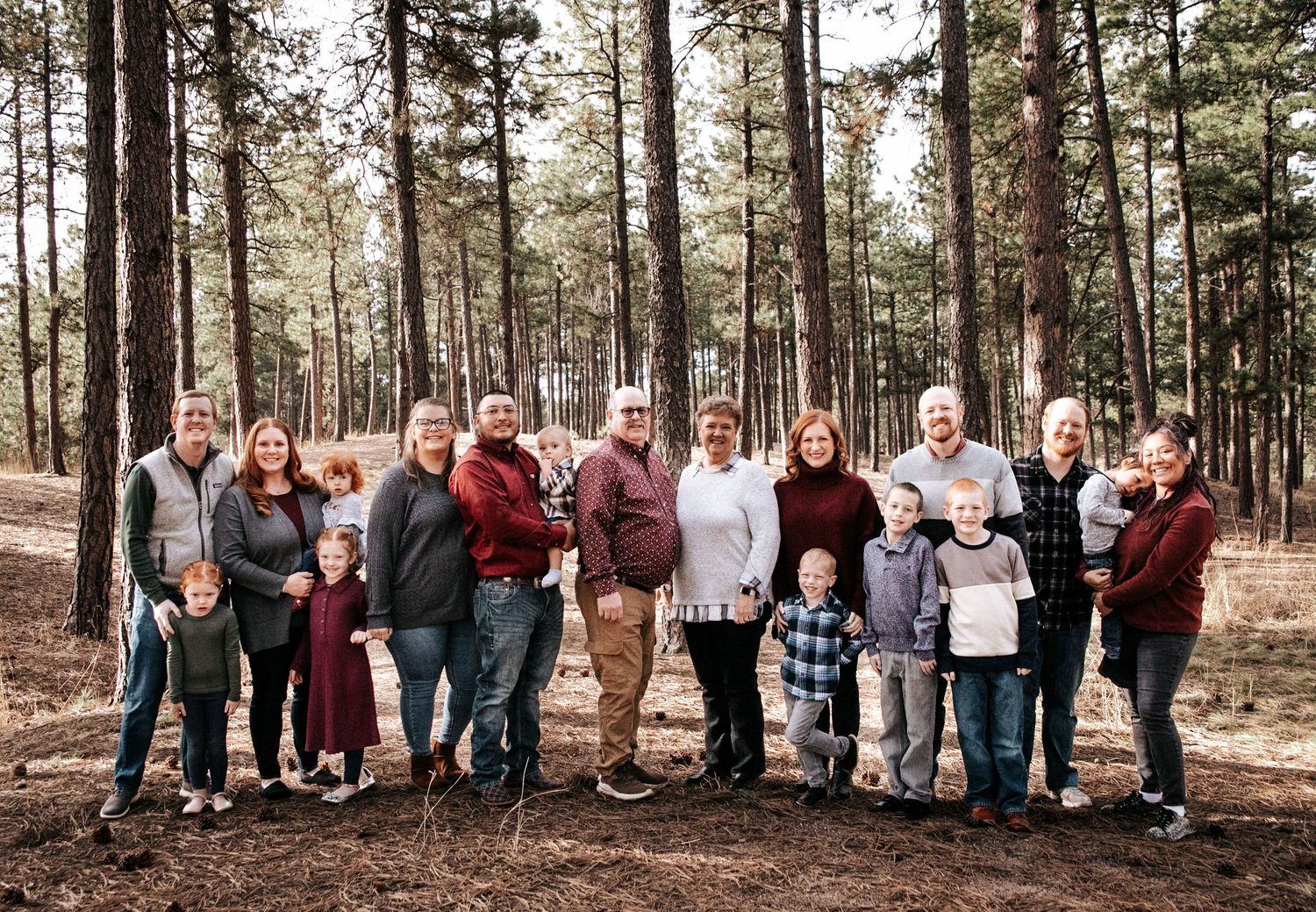 Large family gathering poses together in a pine forest landscape.