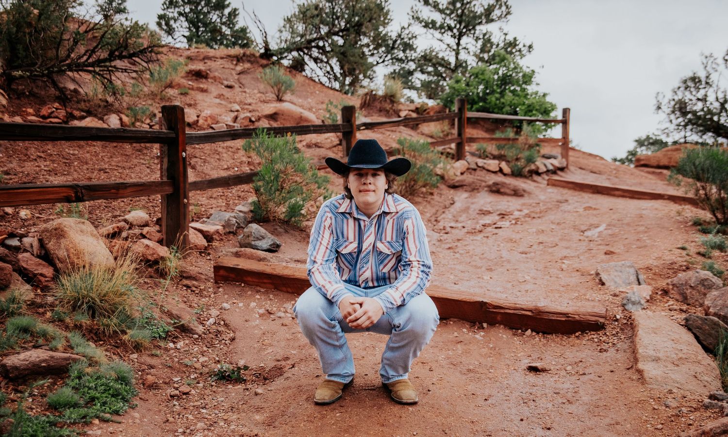 A high school senior crouches on red rock steps at Garden of the Gods in Colorado Springs