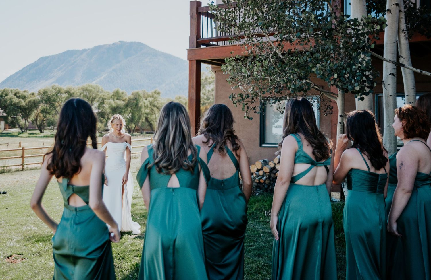 Bridesmaids in matching teal dresses stand together outdoors with mountains in the background.