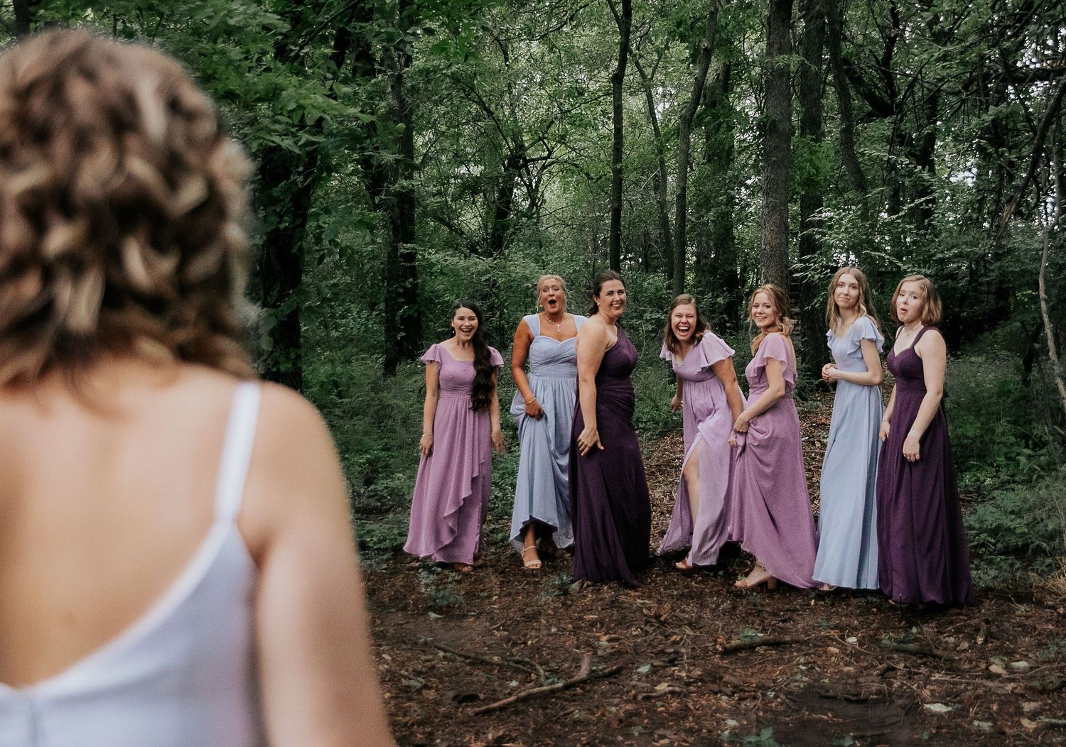 Bridesmaids in lavender and purple dresses posed together in a forest setting.