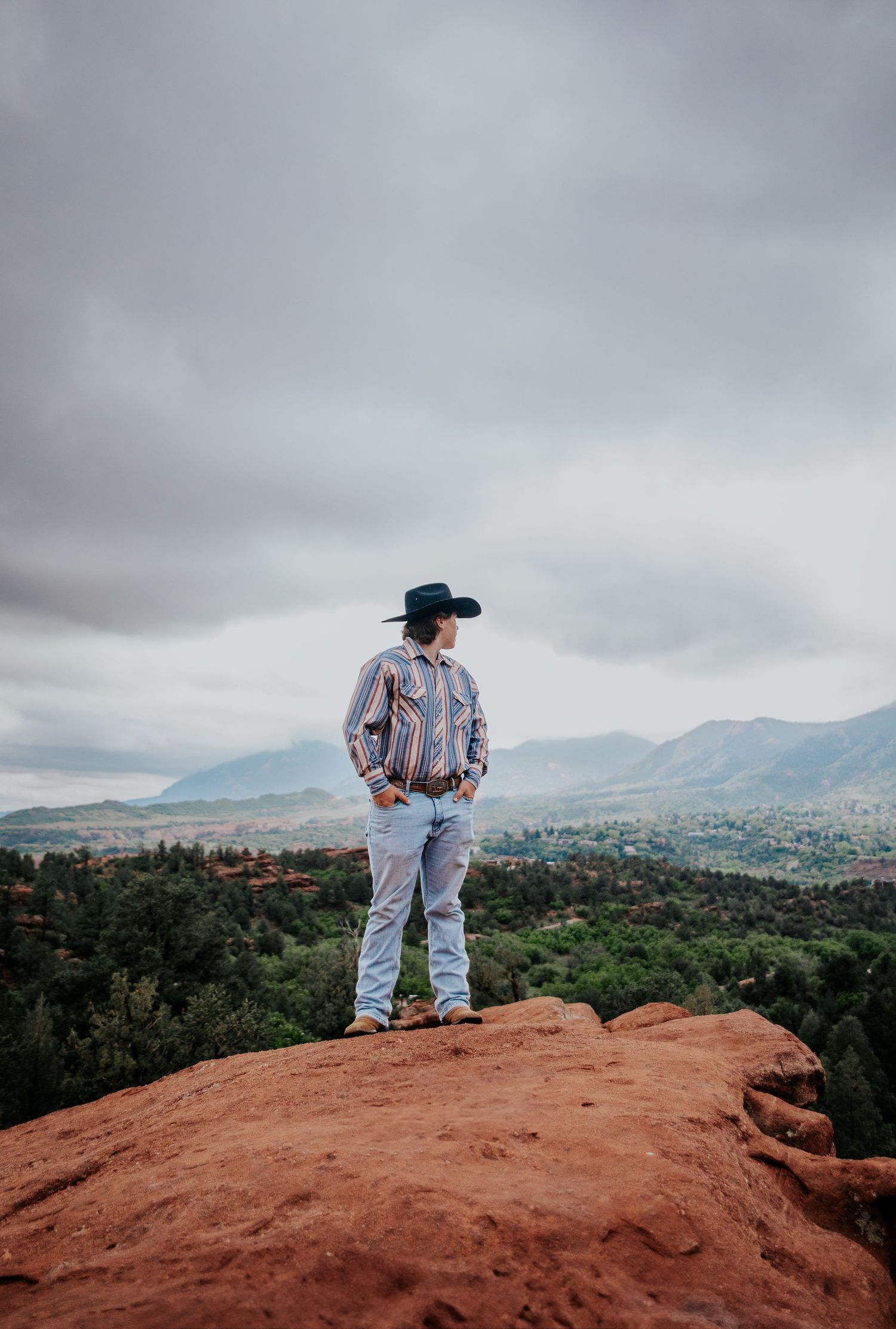 A western-clad figure overlooks a scenic mountain valley from red rocks at Garden of the Gods in Colorado Springs