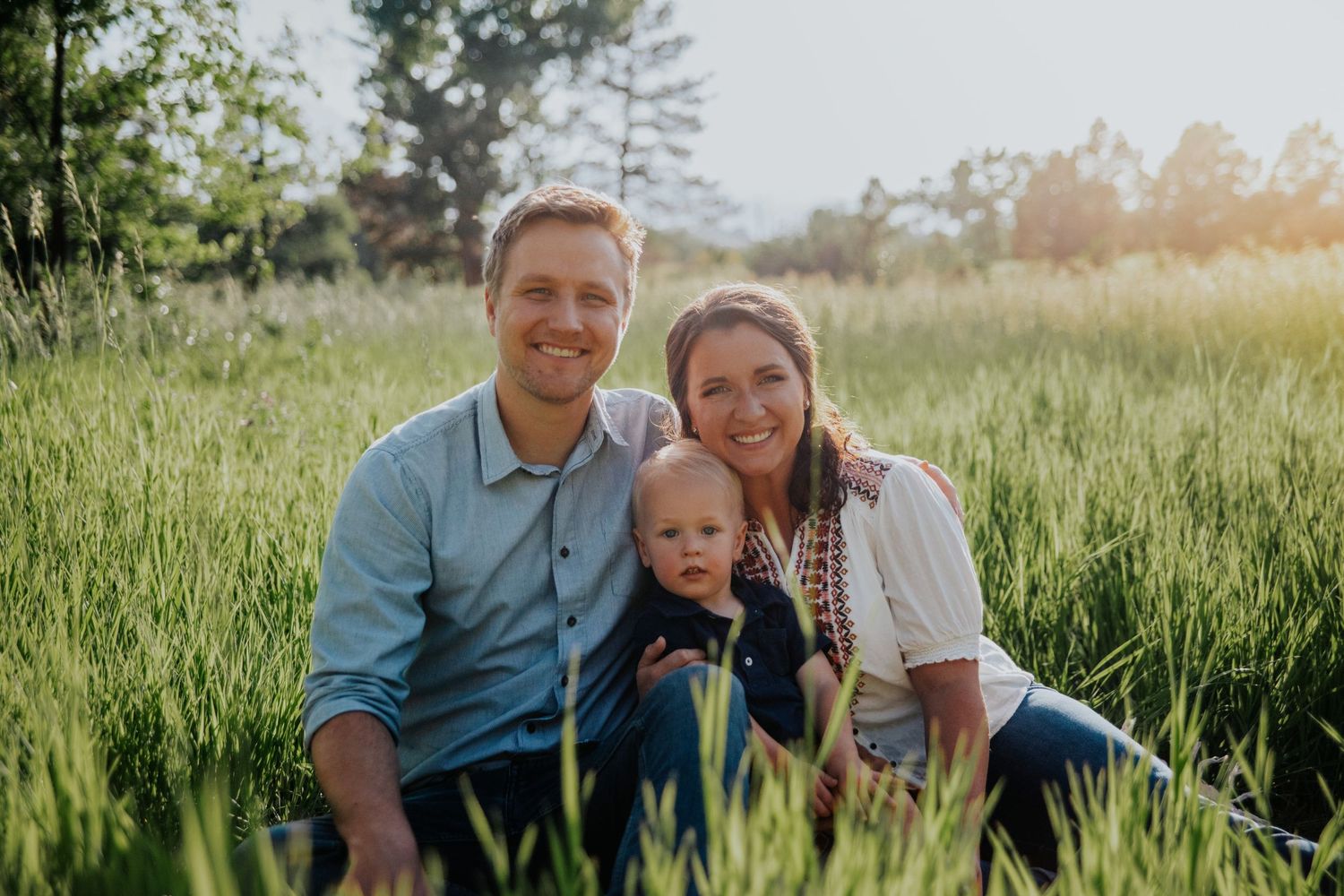 Family relaxing together in tall green grass during golden hour.