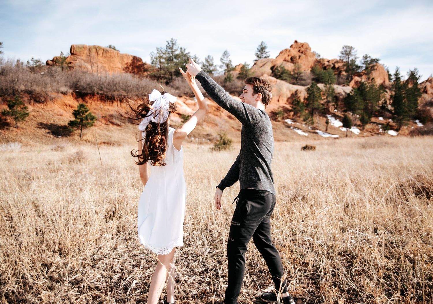 Couple dancing in grasses with red rocks behind at Red Rock Open space during engagement photos in Colorado Springs