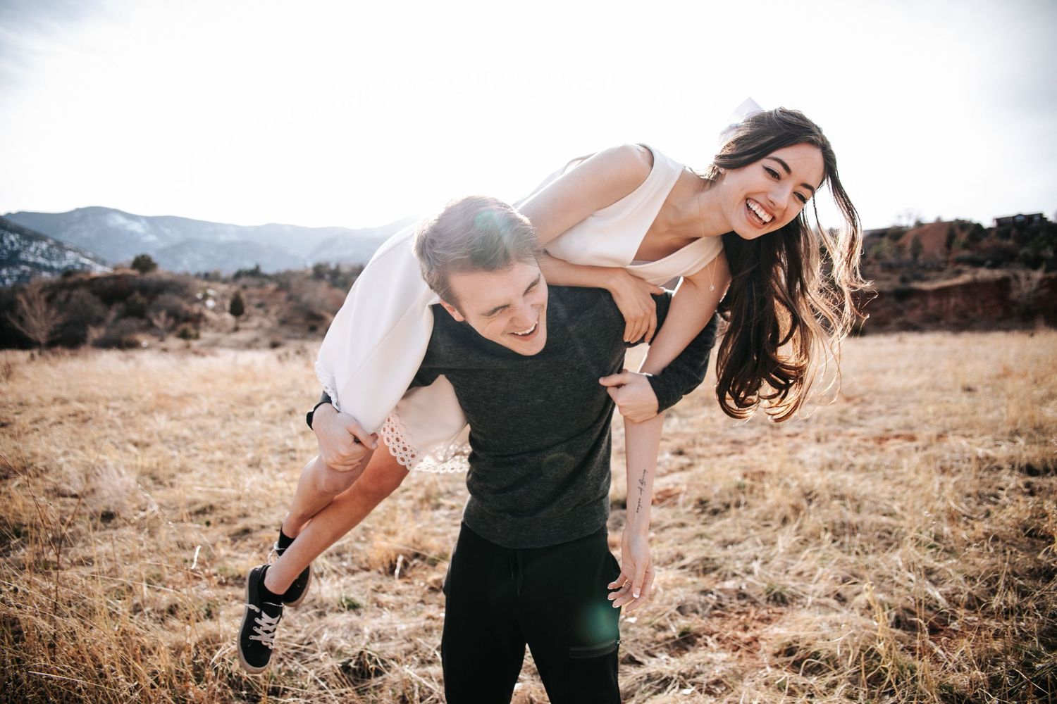 A playful couple enjoys a piggyback ride in a mountain field.