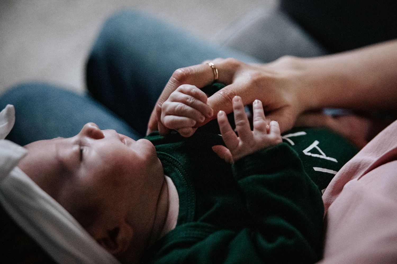 Close up view of tiny baby fingers grasping an adult hand while wearing a dark green outfit.