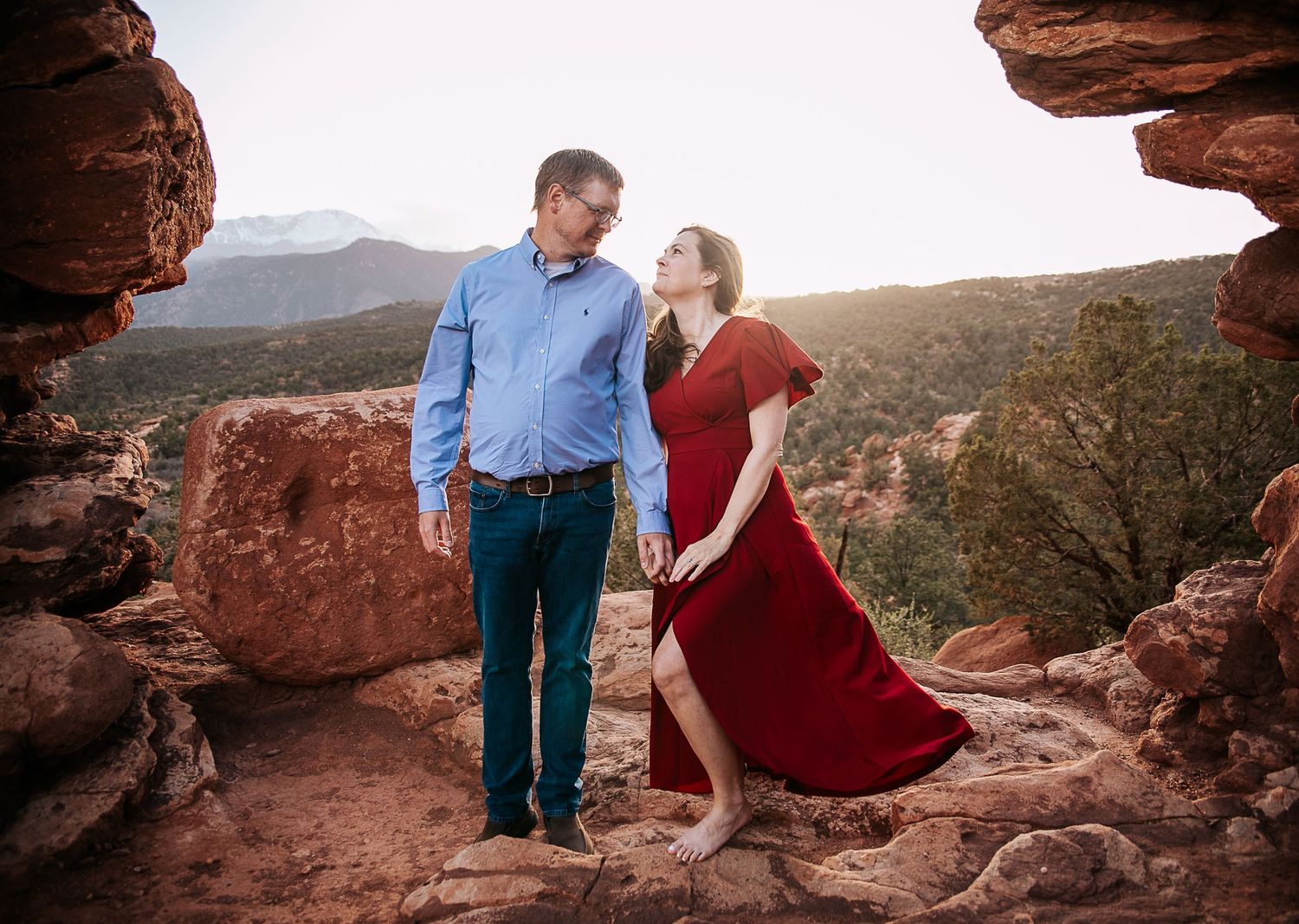 A couple sharing a playful moment on red rocks with mountain views.