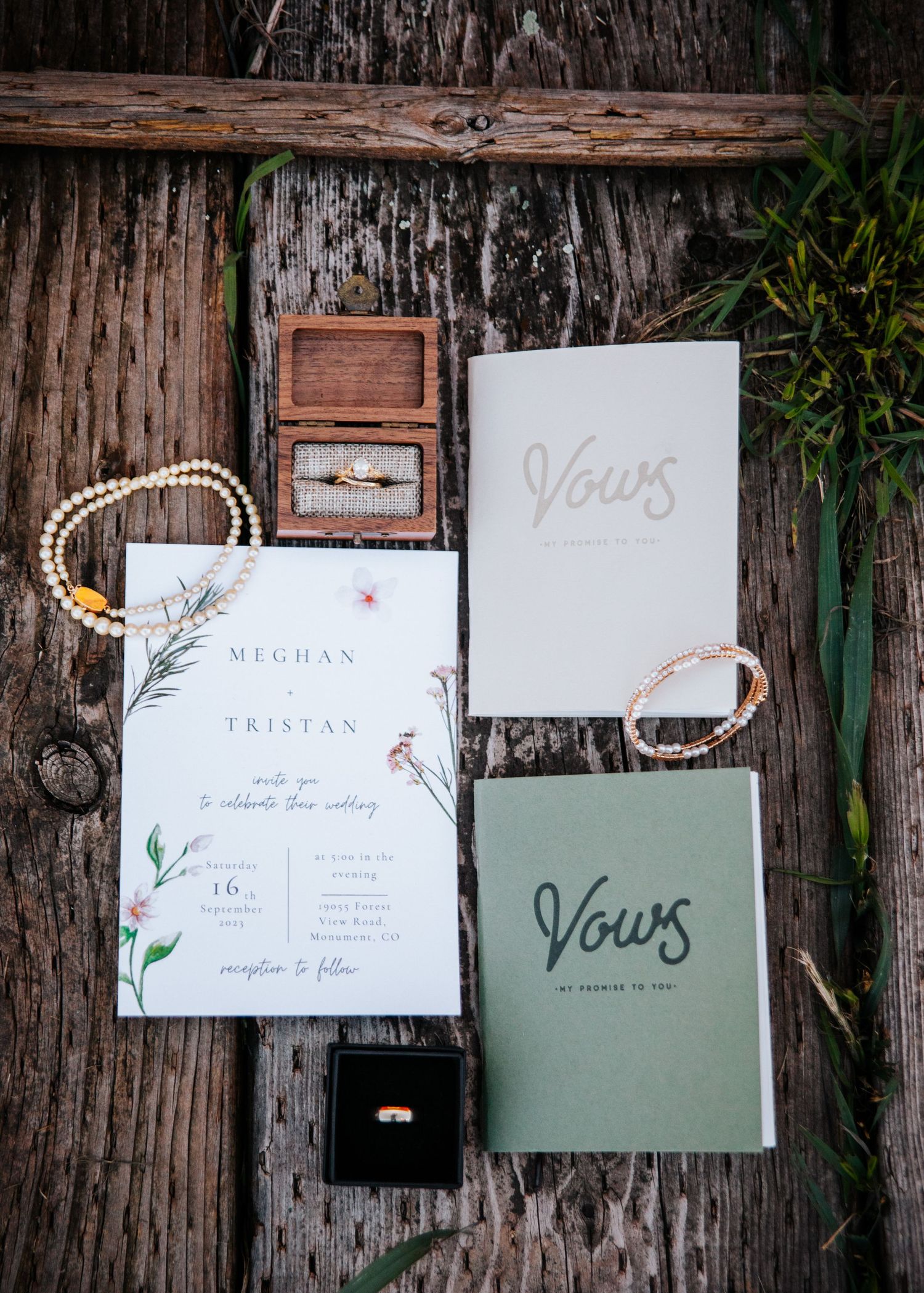 Wedding vow books and invitation suite styled on rustic wooden surface with pearl accessories.