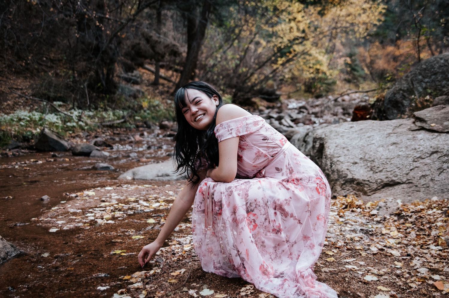 A pink floral dress contrasts beautifully against rocky autumn terrain during an outdoor photoshoot.