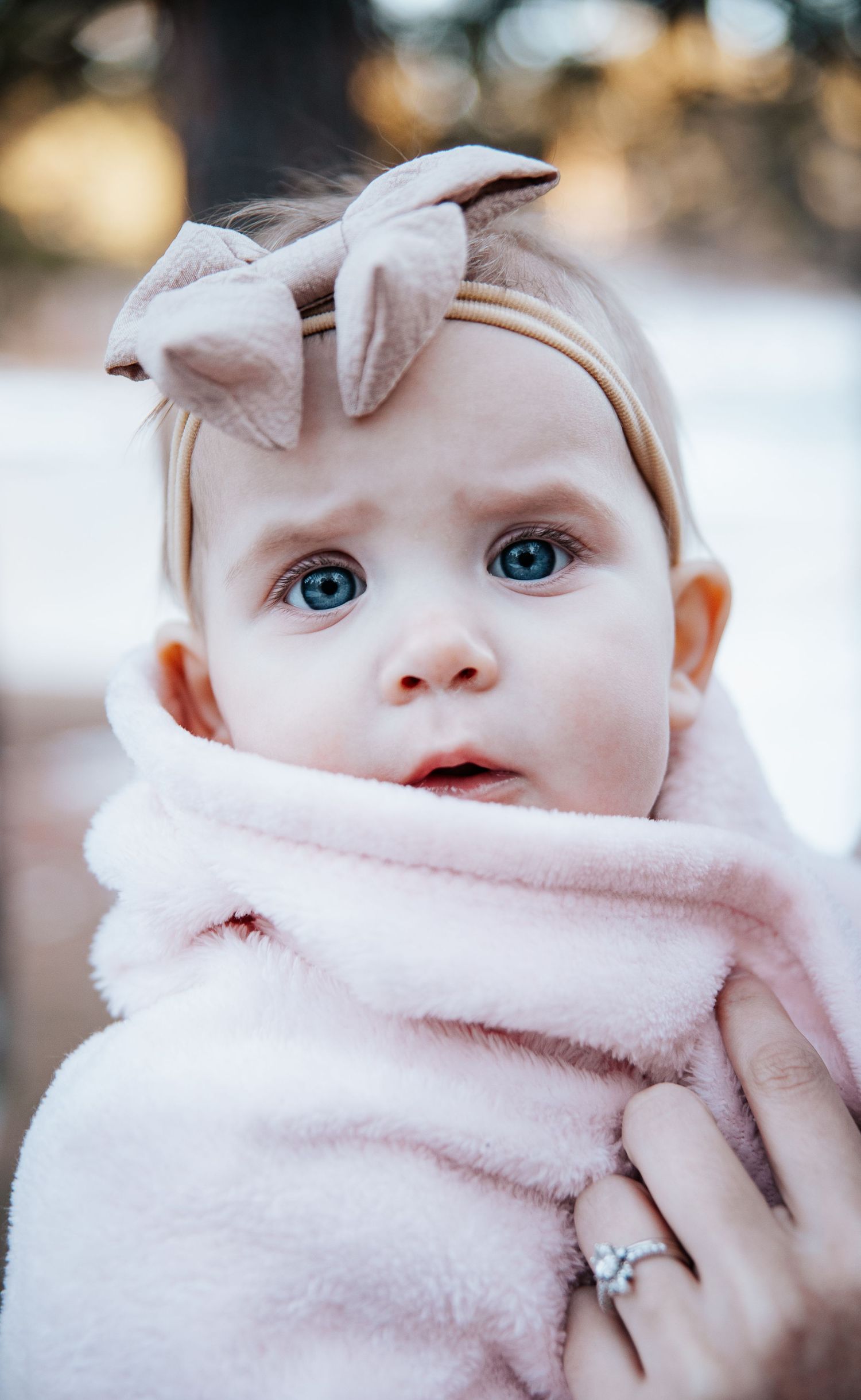 Baby wearing soft pink headband and scarf wrapped snugly in winter attire.