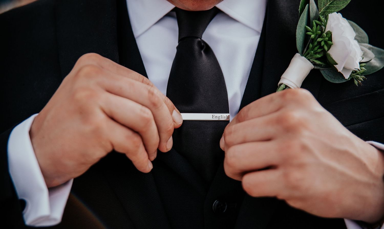 Close-up of hands adjusting a black tie with a white boutonniere on a formal suit.