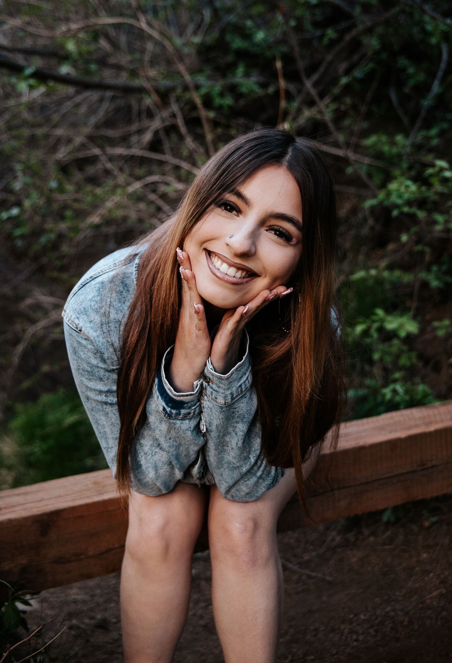 Portrait leaning on wooden railing in forest setting wearing denim jacket.