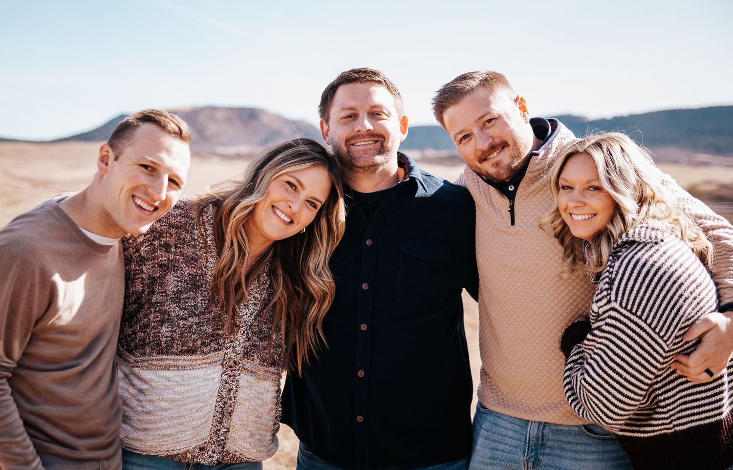 Group of friends laughing and embracing while enjoying a sunset together outdoors.