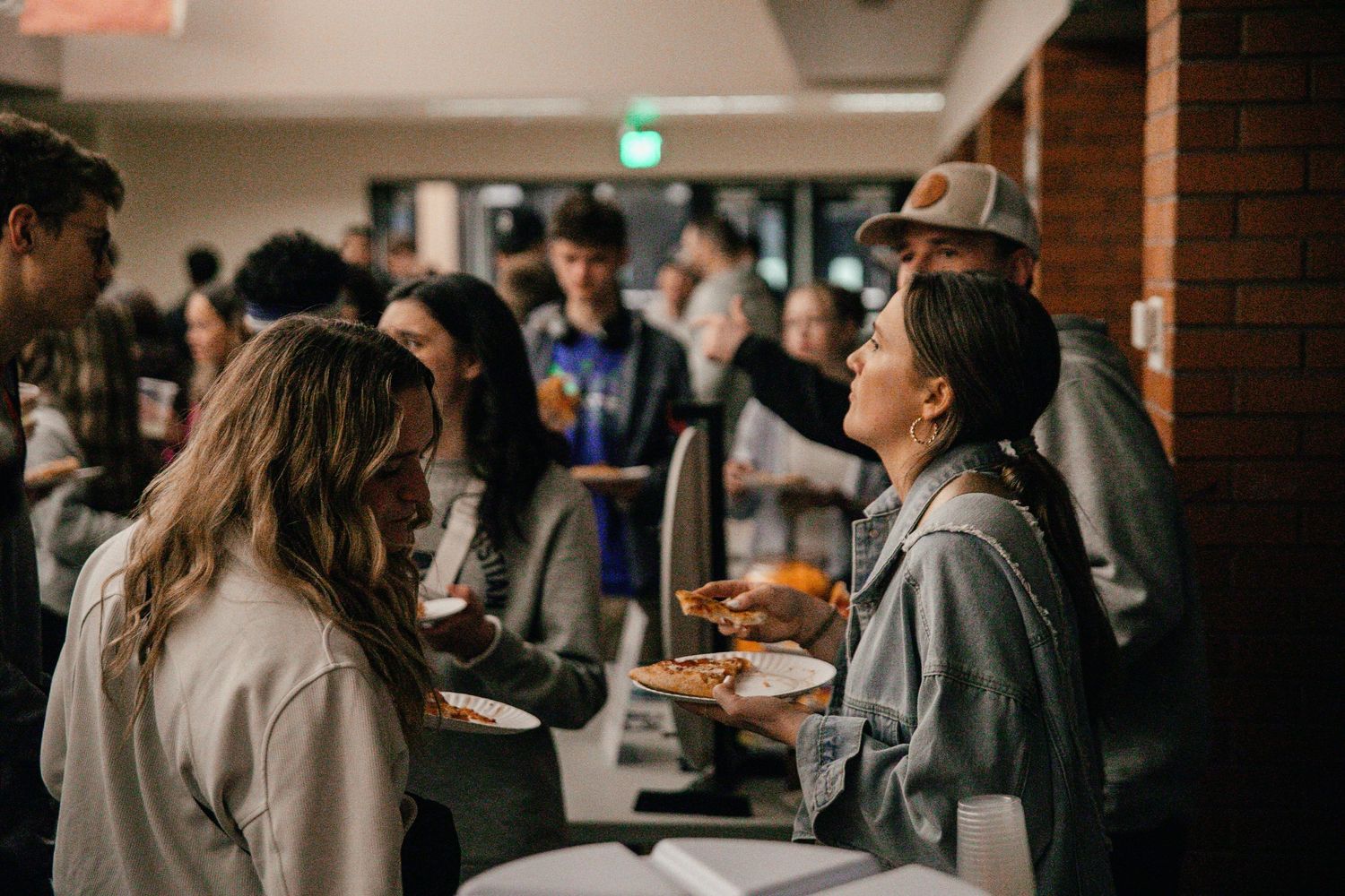 Large group mingling in a brick-walled room during a casual gathering.