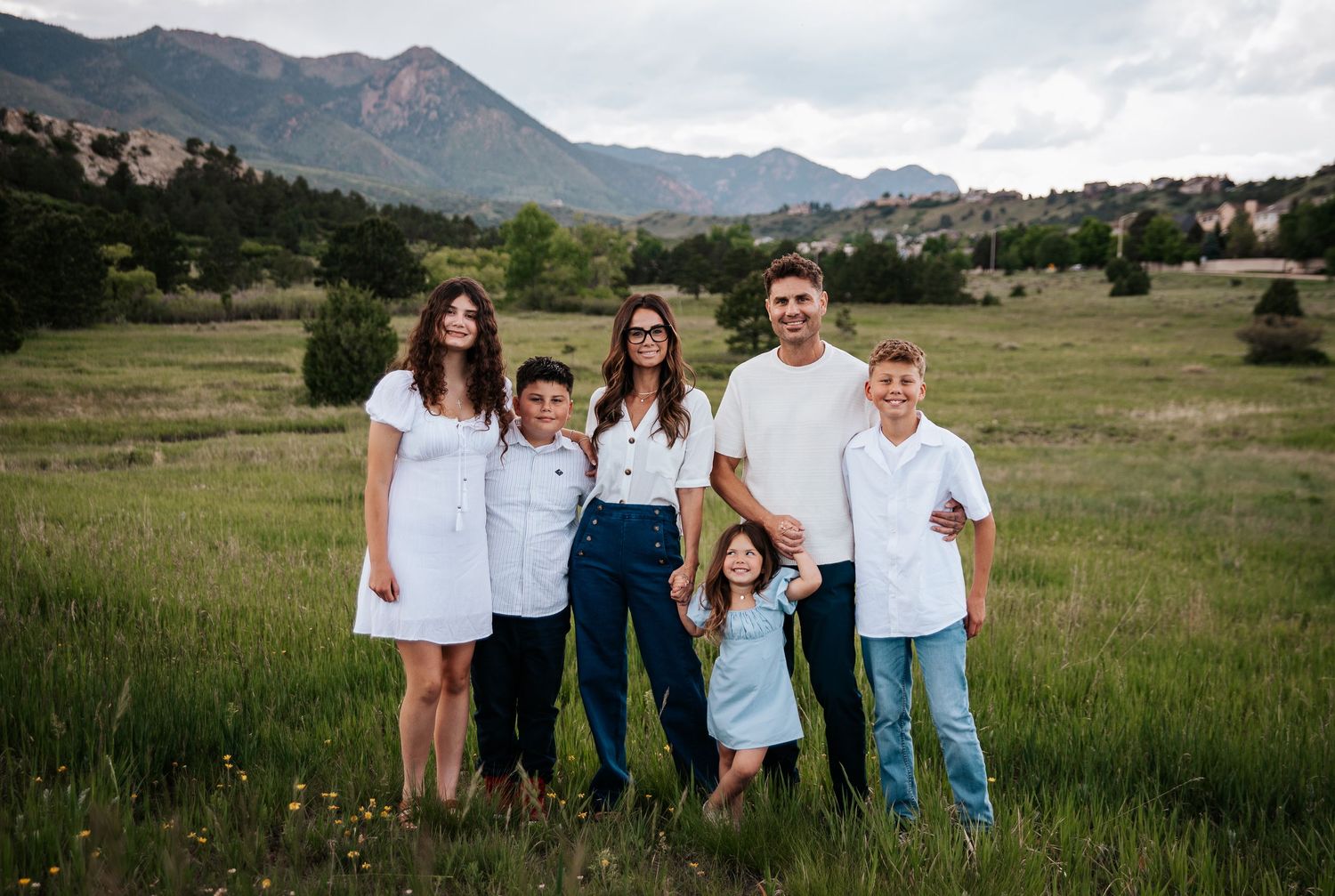 Family group stands together in open field with Rocky Mountains visible in background at Ute Valley Park in Colorado Springs