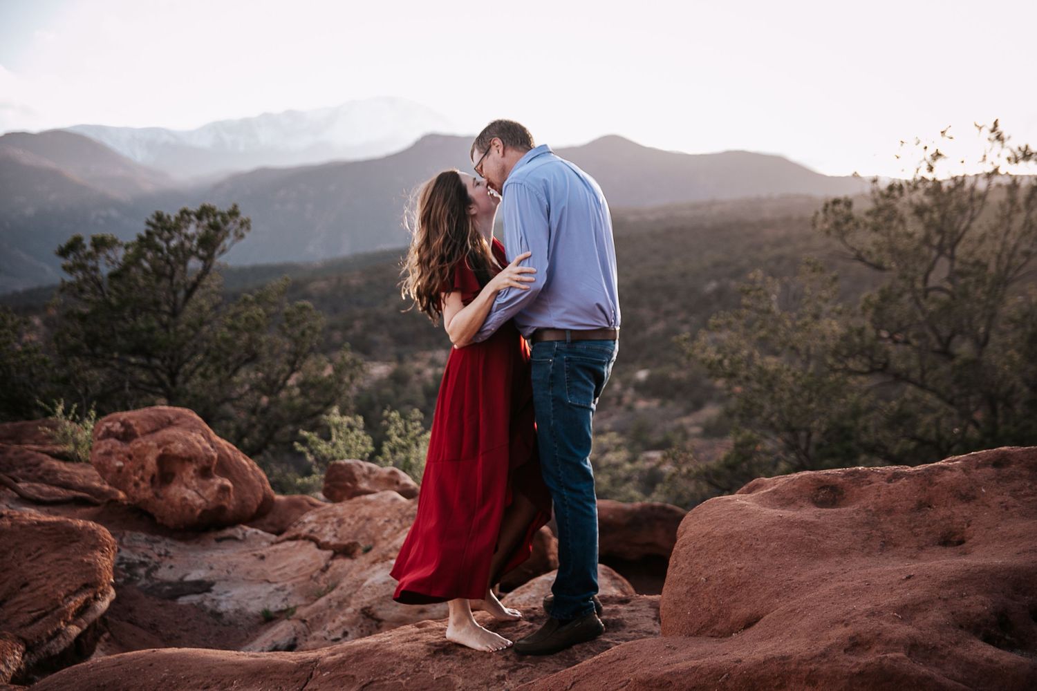 A romantic moment captured on red rocks with mountains and desert landscape in the background.