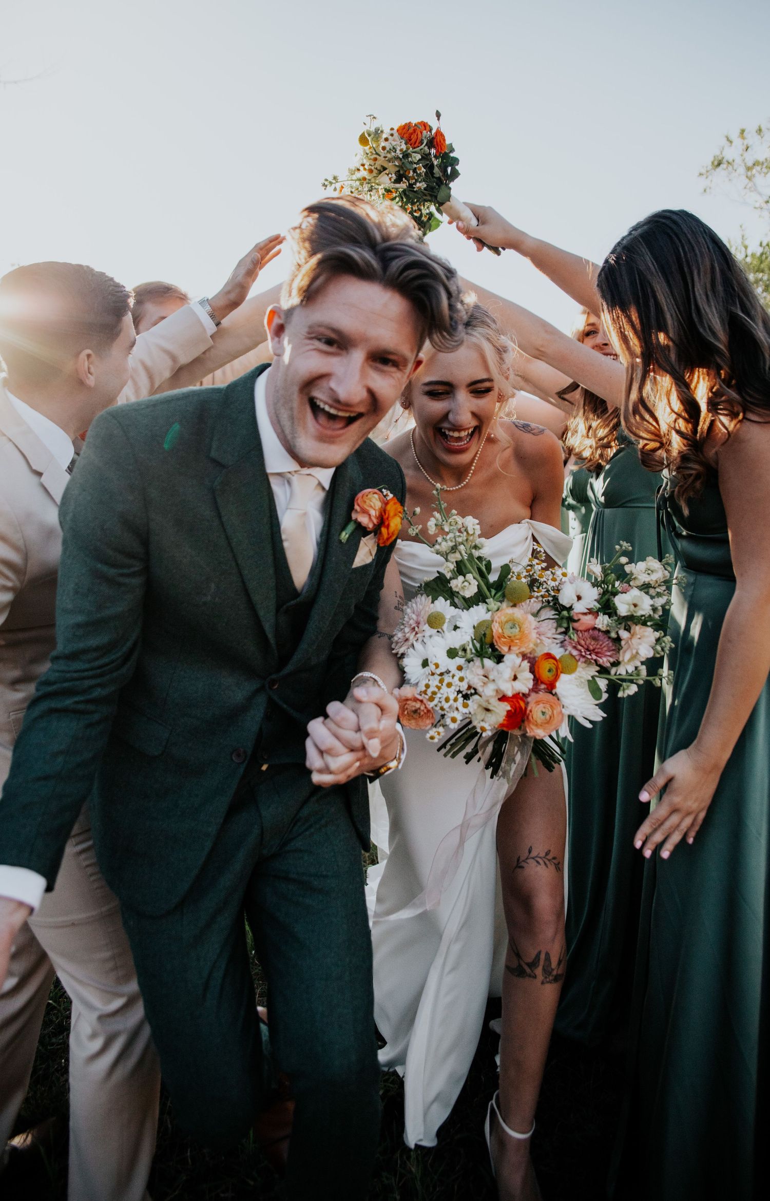 Wedding party laughing together in formal attire with bridesmaids in dark green dresses.