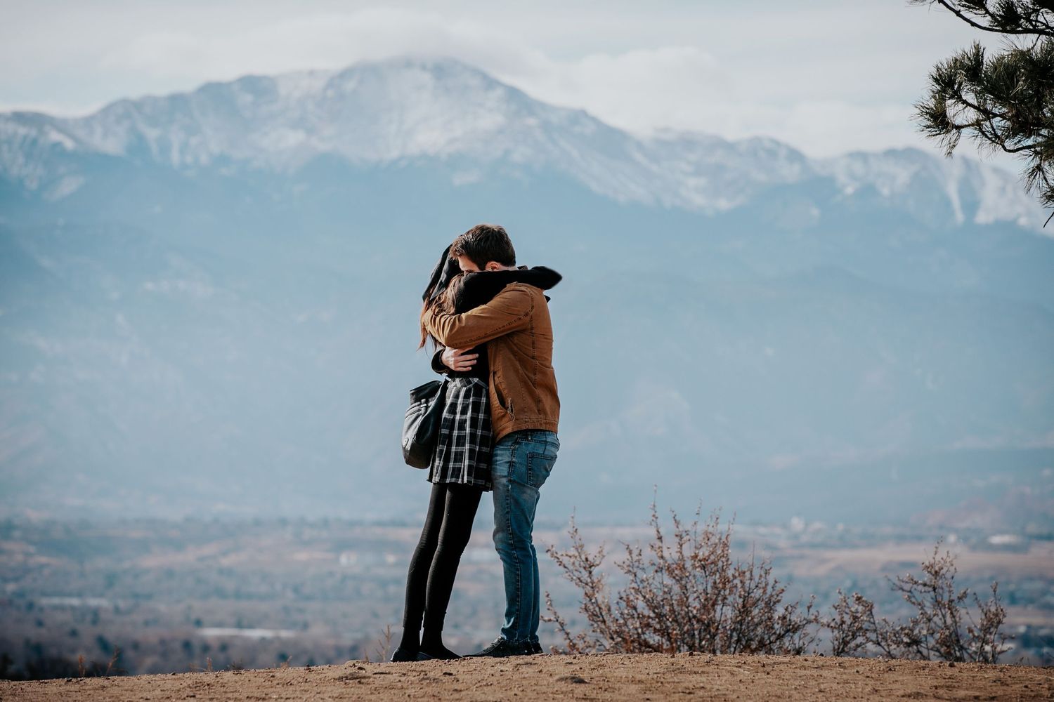 Two people embrace while enjoying scenic mountain views from hilltop overlook.