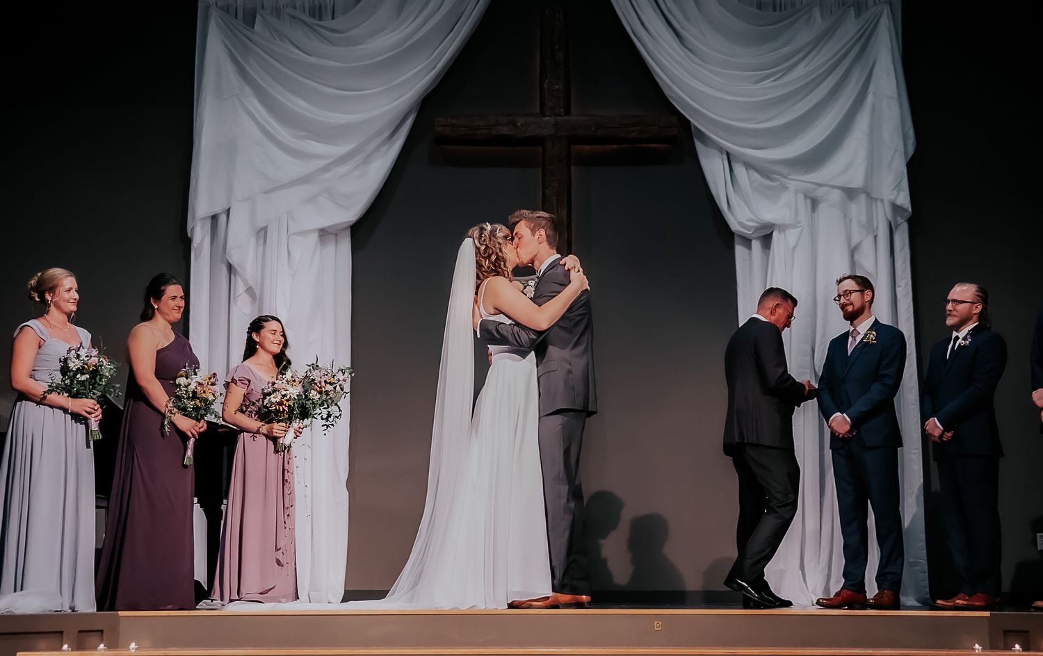 Wedding ceremony under white draped arch with wedding party in formal attire.