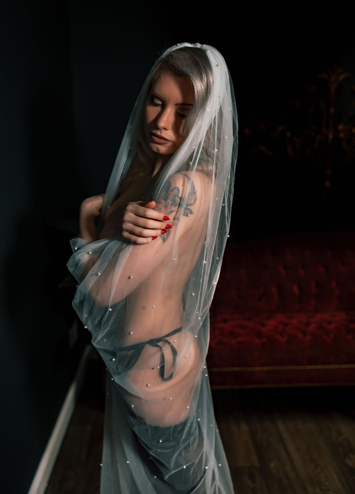 Artistic bridal boudoir photo of a topless woman with flowing white sheer veil against dark background featuring black lace lingerie.