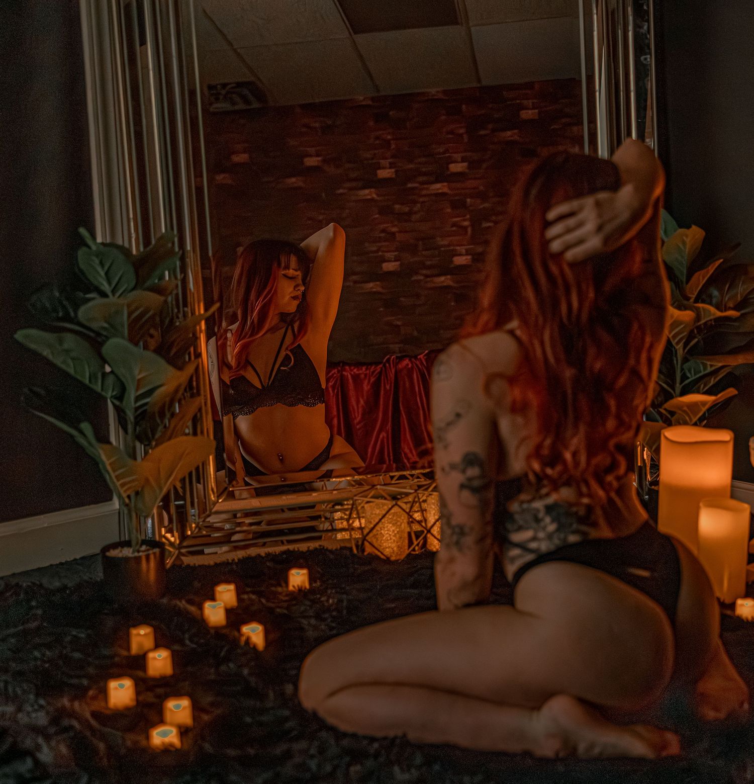 A boudoir photo of woman in black lingerie in candlelit scene kneeling with mirror reflections, featuring candles and mirror
