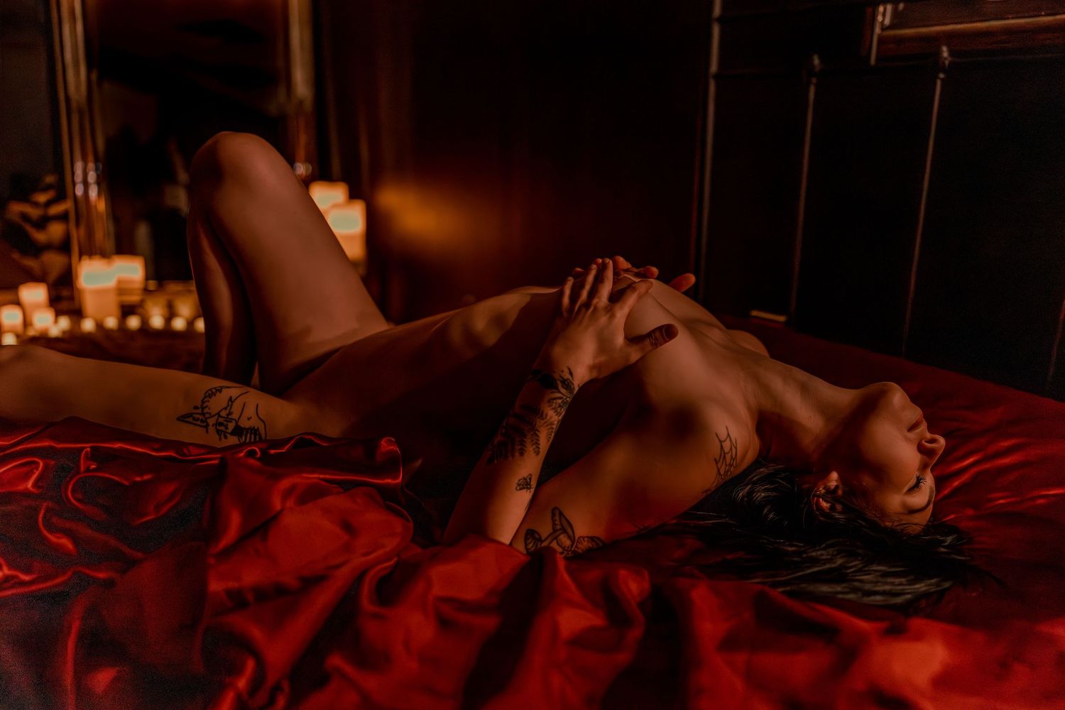 Candlelit erotic nude boudoir scene with women posed nude red satin sheets in romantic setting and intimate pose.