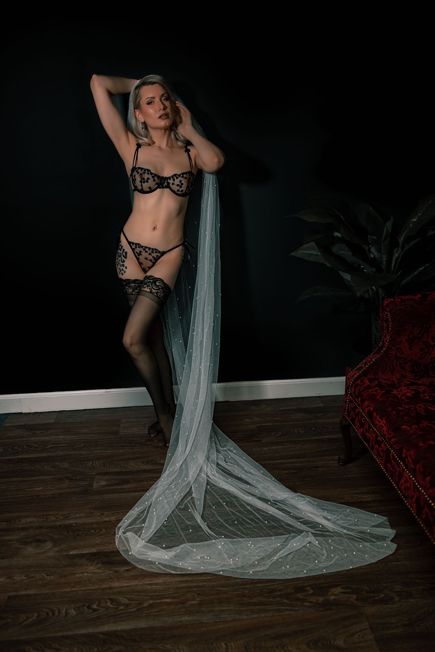 Artistic bridal boudoir photo of a woman with flowing white sheer veil against dark background featuring black lace lingerie.