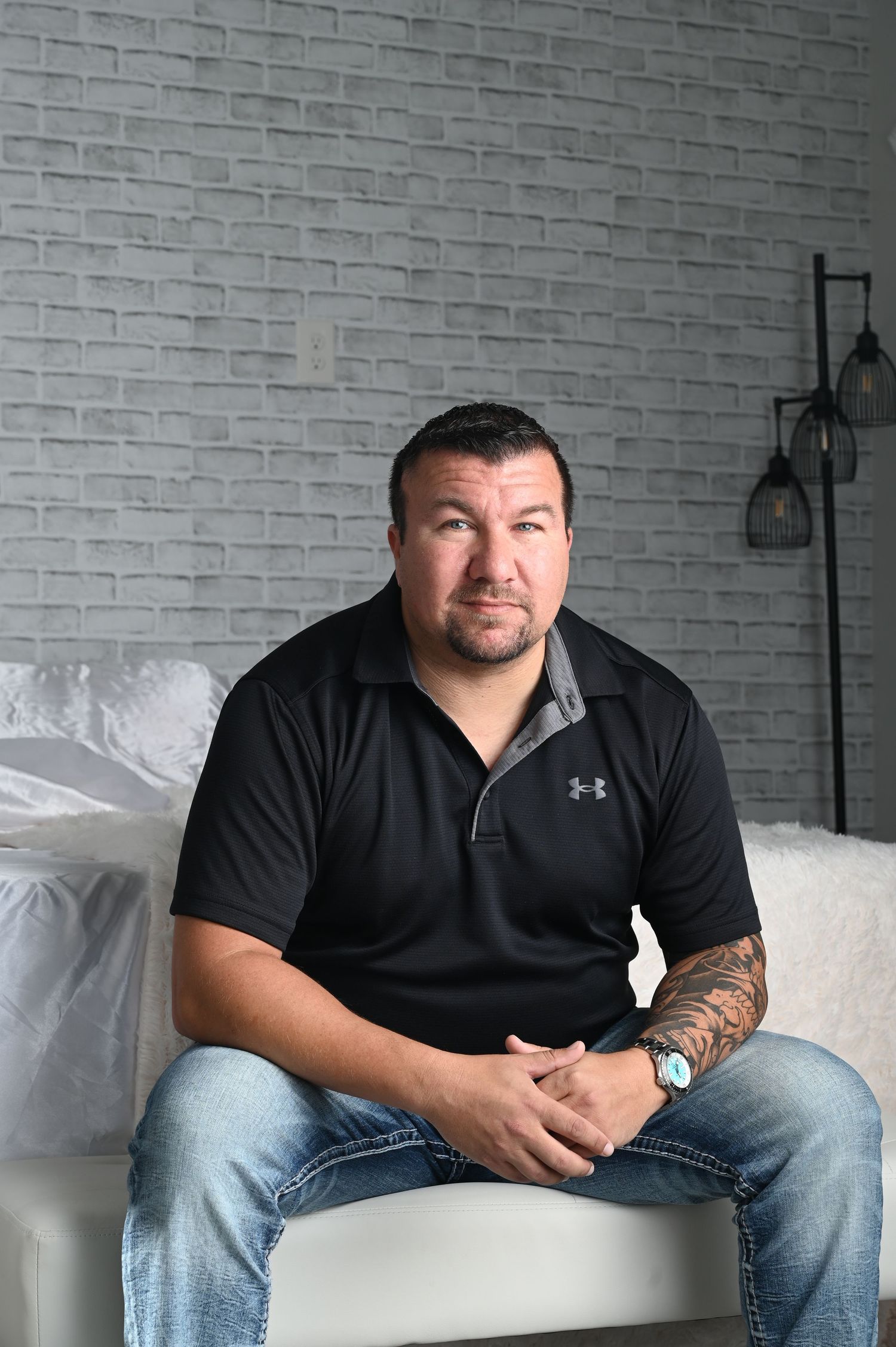 Person wearing Under Armour shirt seated casually on white sofa with brick wall backdrop.