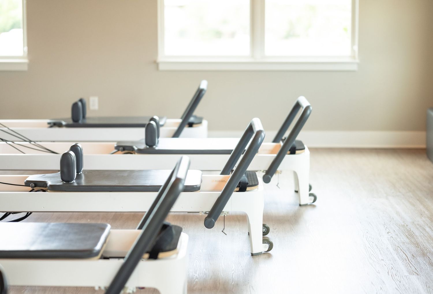 Multiple Pilates reformer machines lined up in a sunlit fitness studio with hardwood floors.