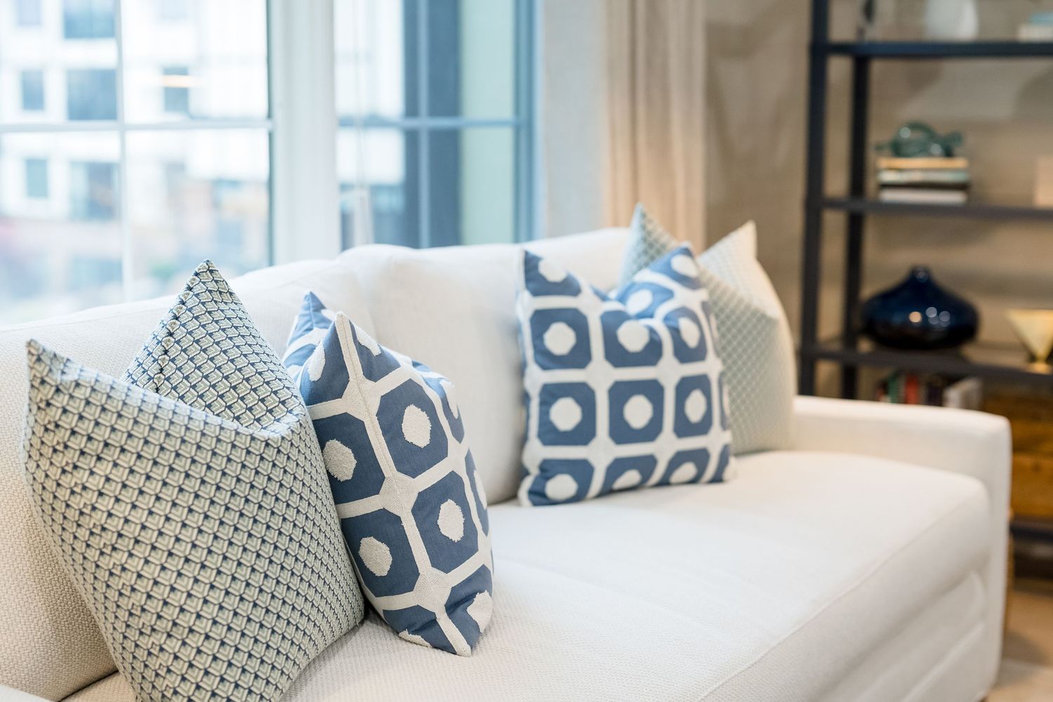 Modern living room interior with white sofa and blue geometric pattern throw pillows against a bright wall.