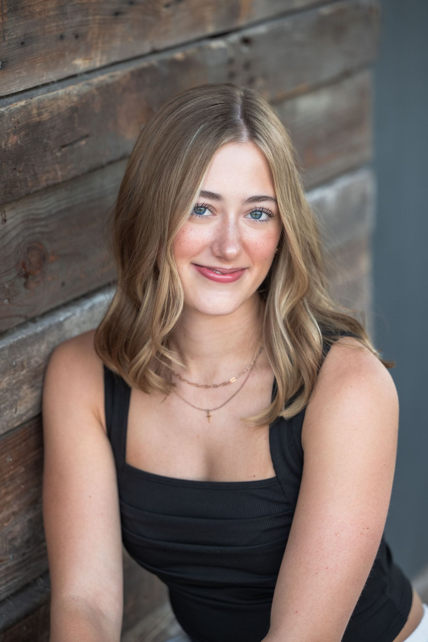 Professional headshot portrait against rustic wood wall background in black sleeveless top.