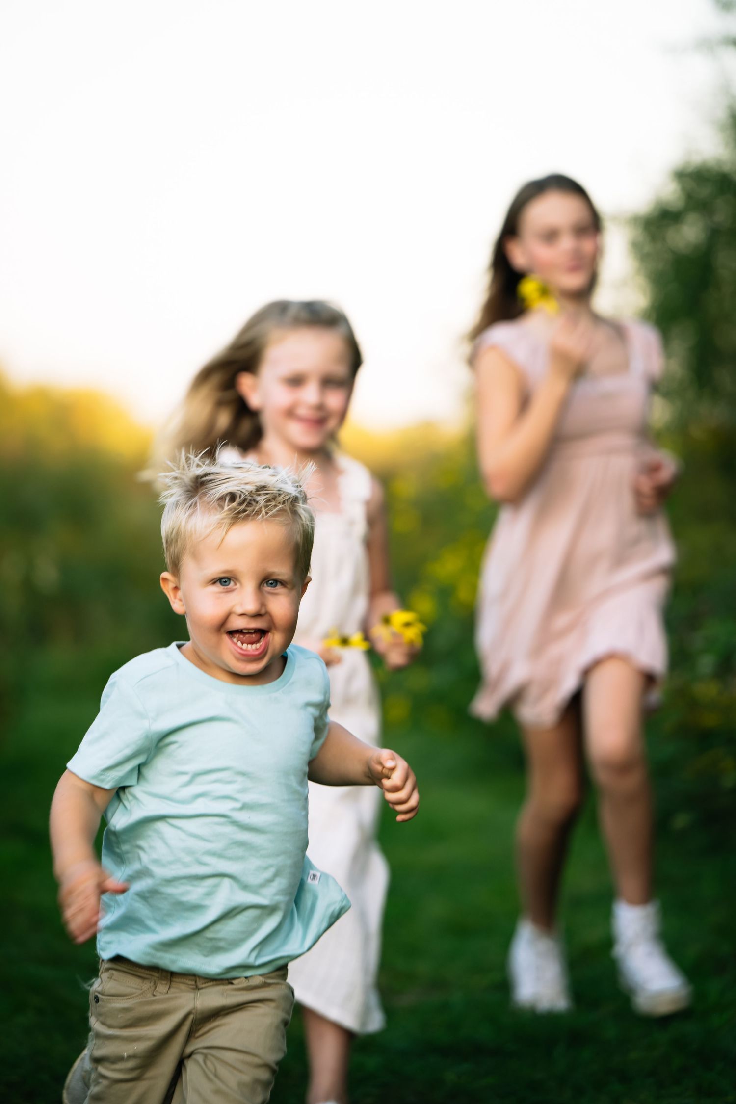 Children playing and running outdoors in a grassy field on a sunny summer evening with dandelion flowers.