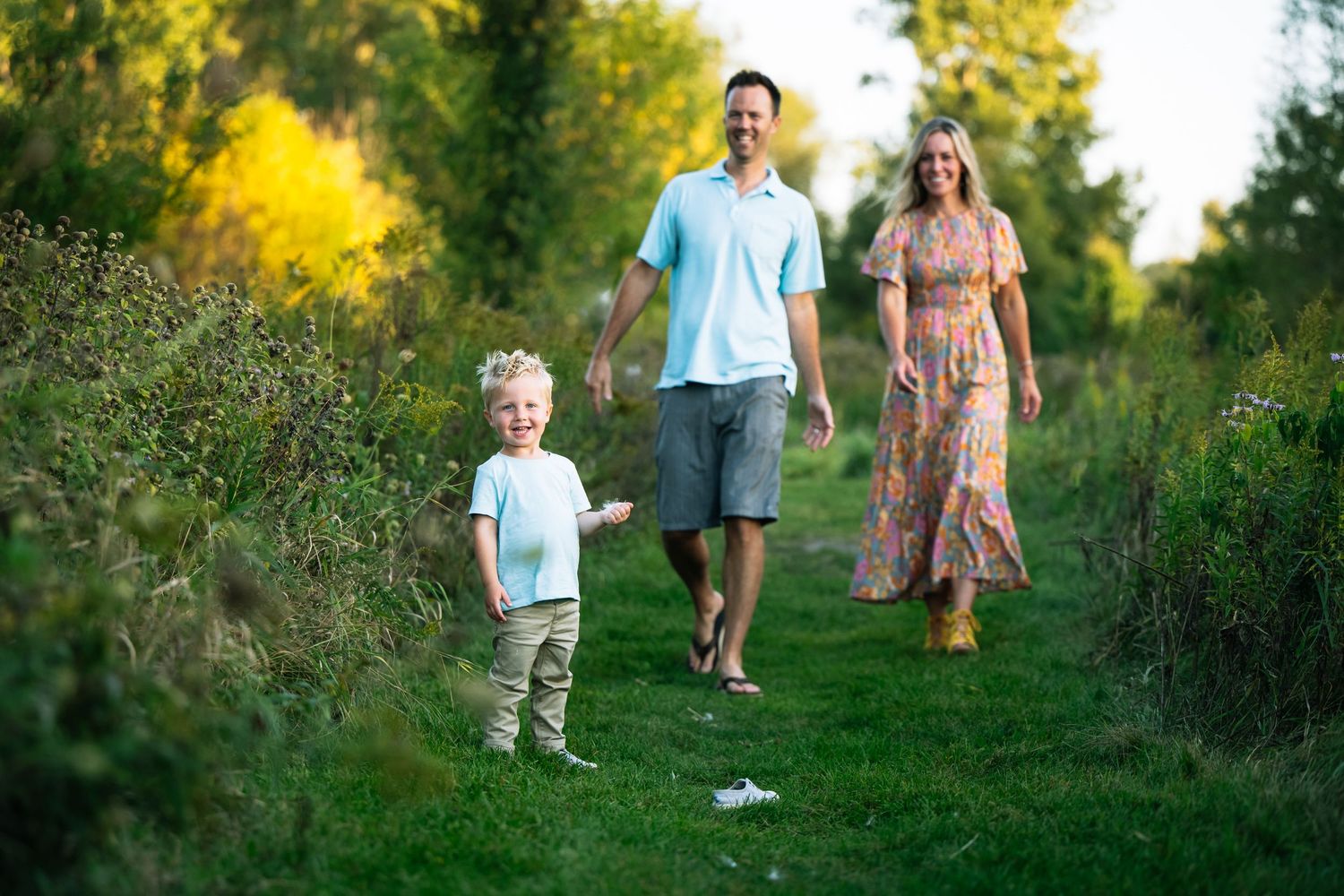 A family walks together on a grassy path surrounded by wildflowers during golden hour in summer.