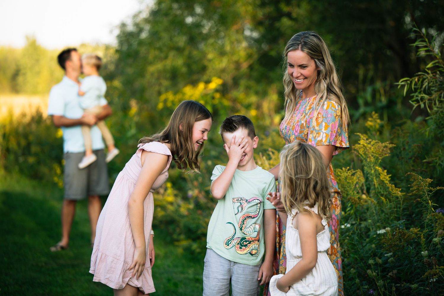 Family group stands together in a golden sunlit garden during sunset creating a warm outdoor portrait session.