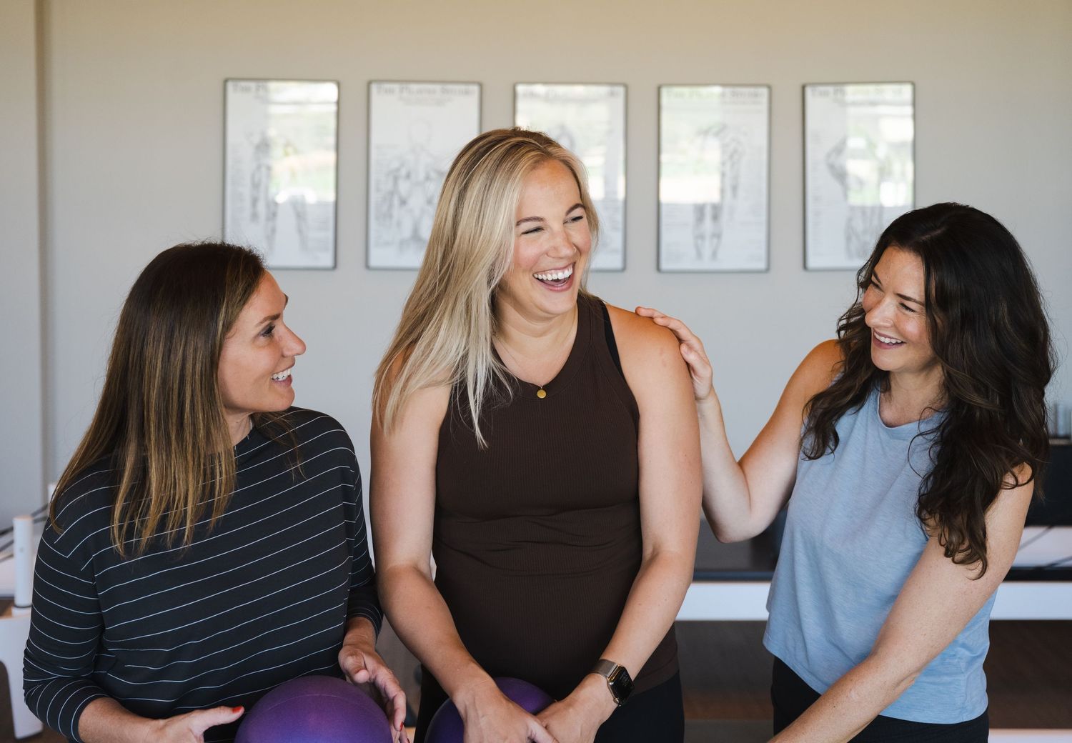A group of women sit together in a row laughing and smiling while socializing indoors.