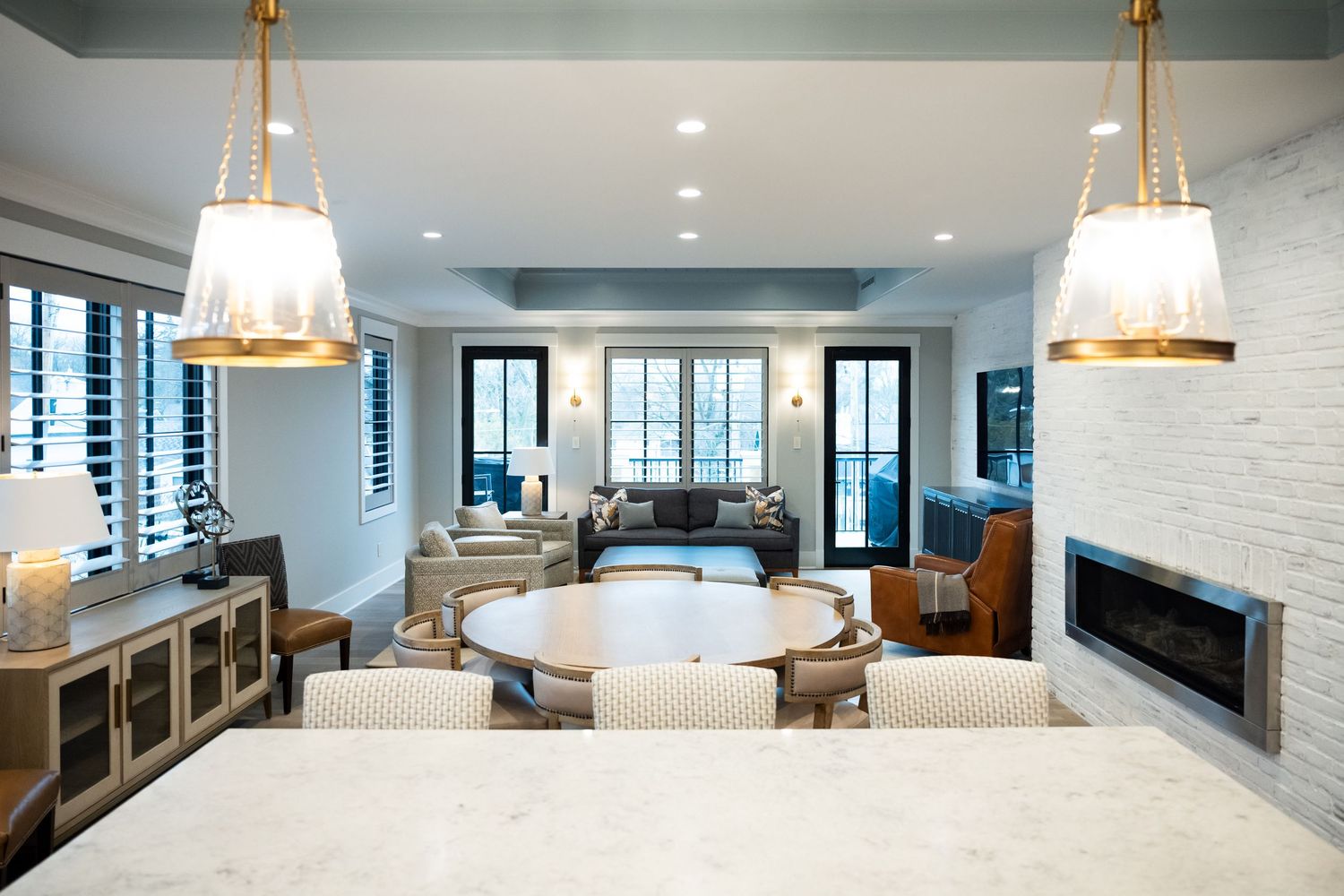 Modern open concept living room with marble countertops, gold pendant lights, and white brick fireplace in coastal style.