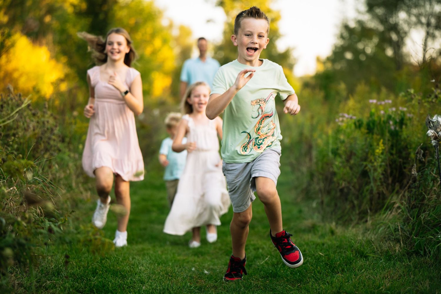 Children running and playing together on a grassy path with golden wildflowers in the background during summer.