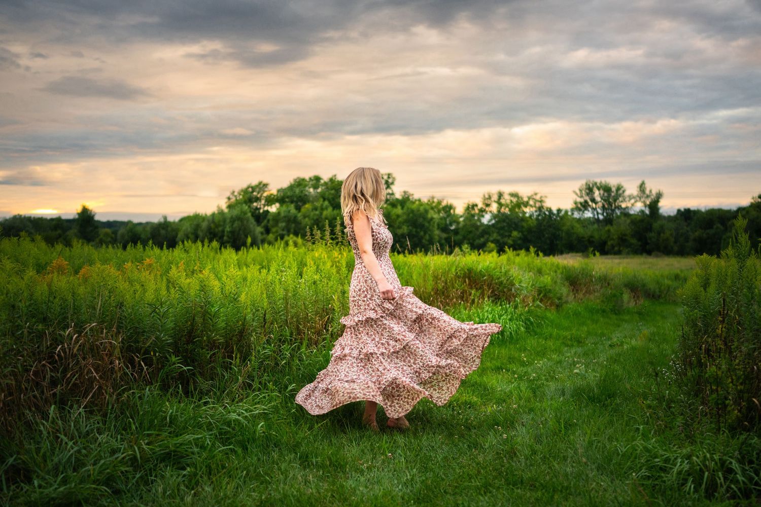 A flowing pink dress floats ethereally across a lush green meadow landscape at sunset.