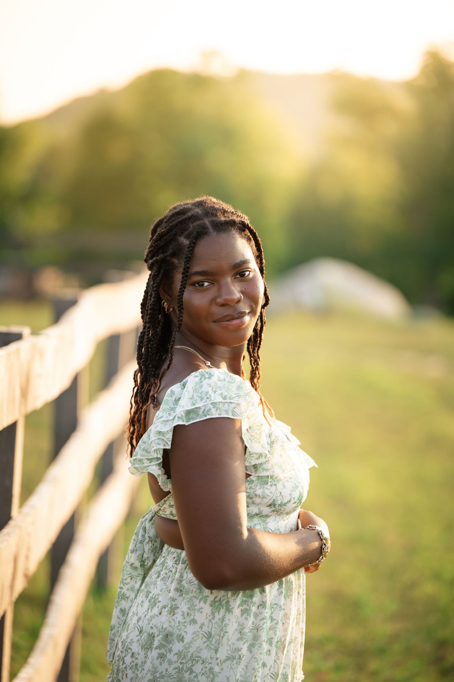 A person in a white lace dress poses against a wooden fence at sunset with warm golden lighting.