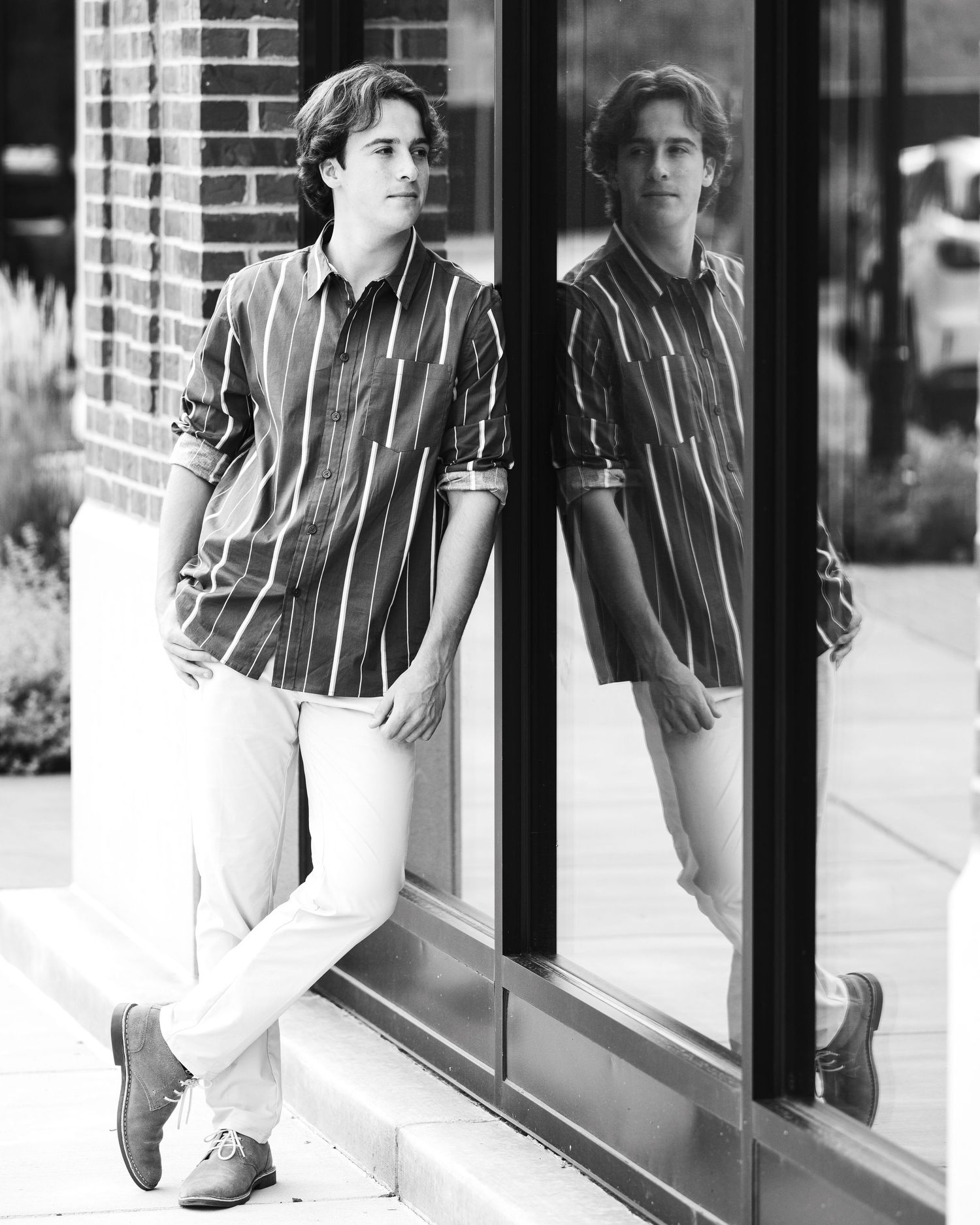 Black and white photo of someone in a striped shirt sitting near a window with a reflective surface.