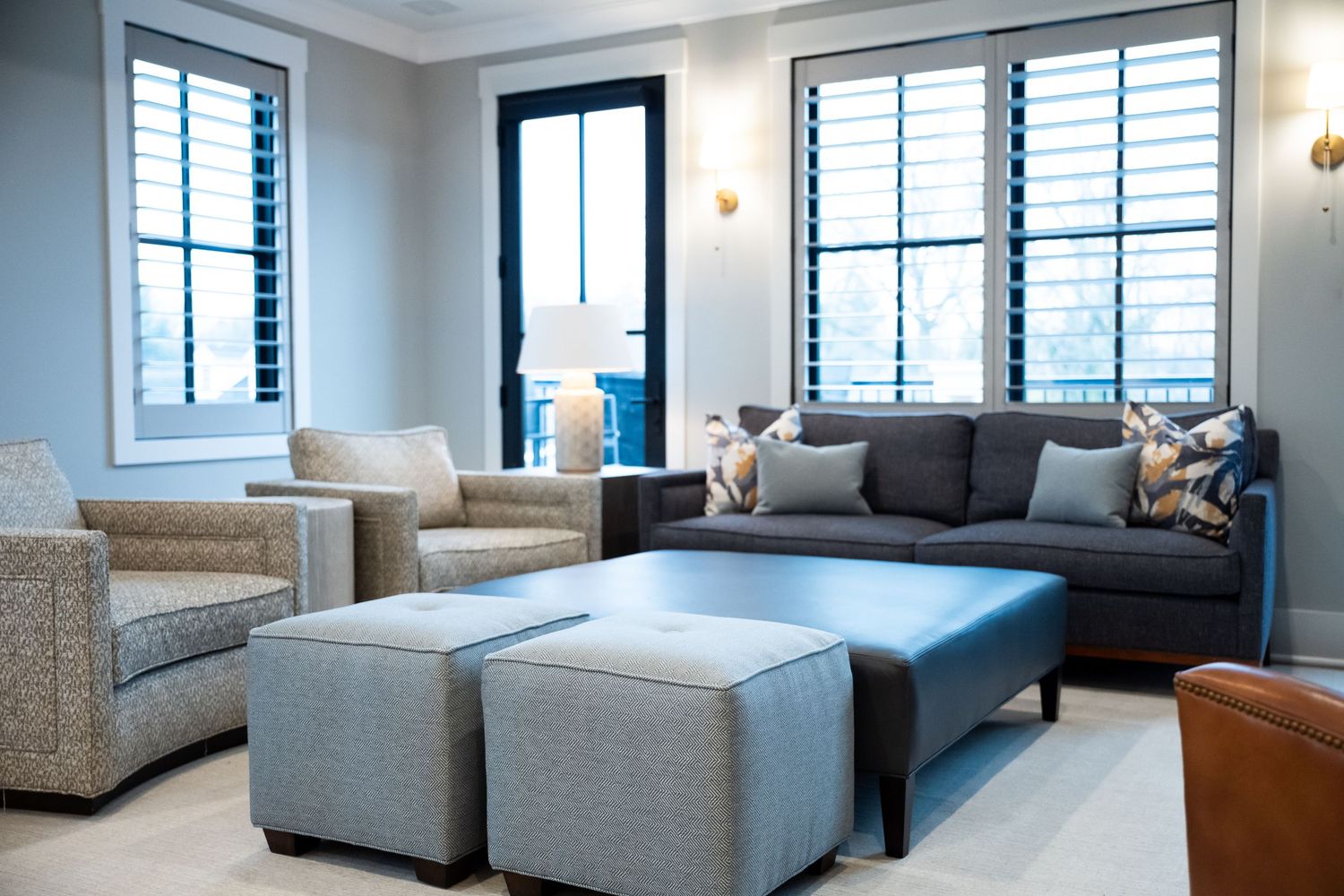 Modern living room interior with gray sectional sofa, white walls and plantation shutters on windows.