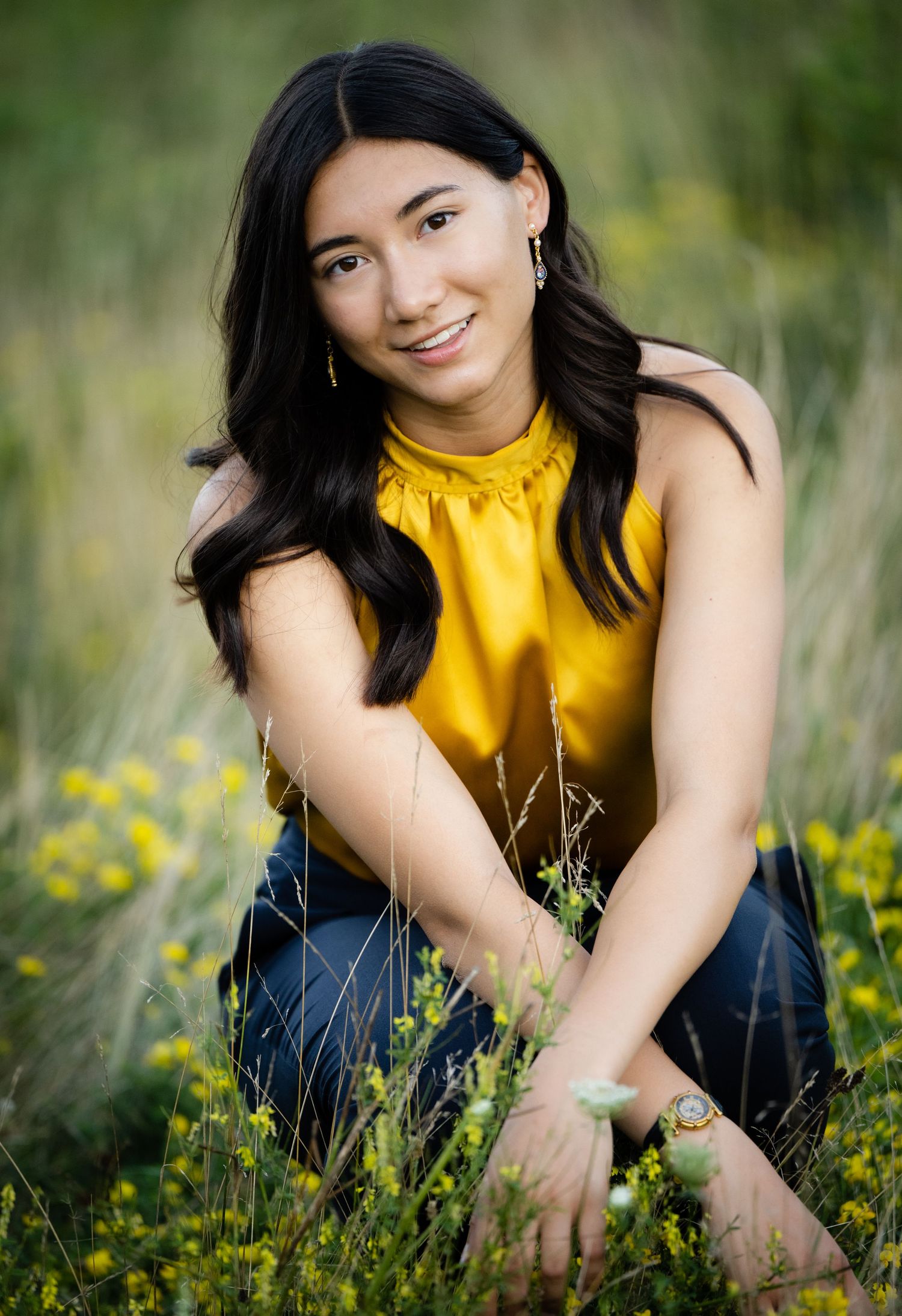 Senior girl in bright yellow top poses in field of yellow wildflowers.