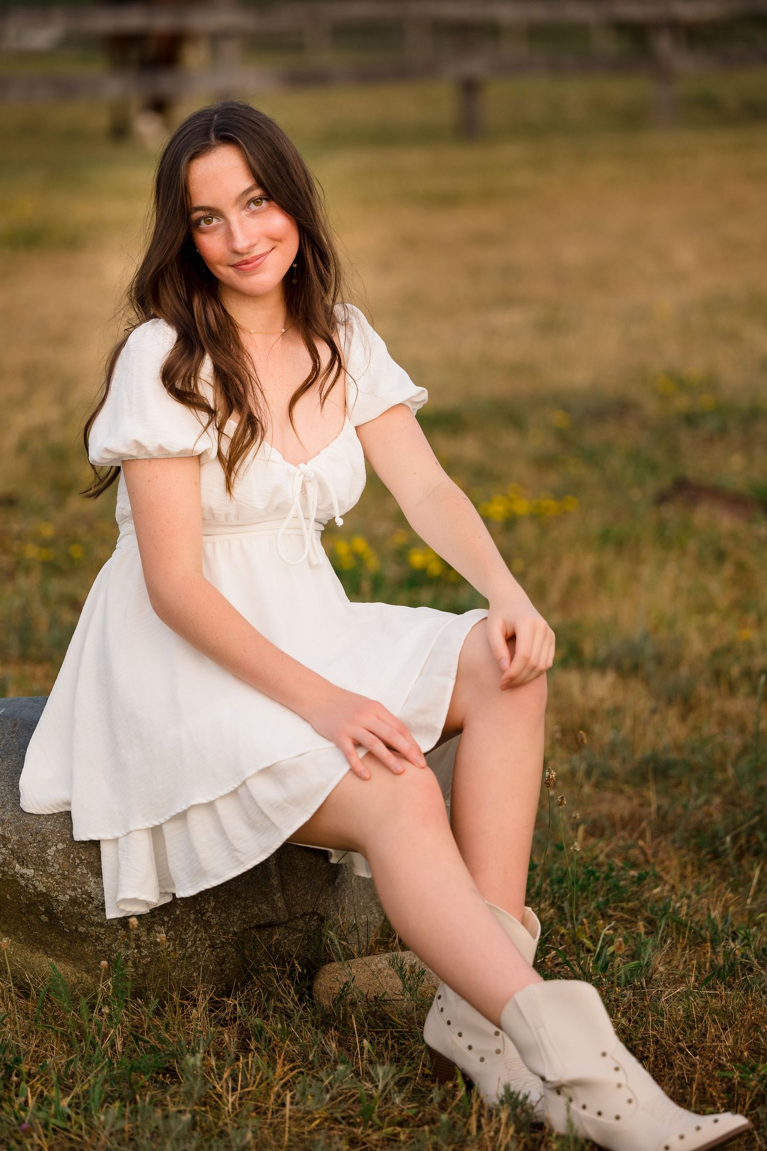 A person in a white dress and white boots poses on grass during golden hour outdoor photography session.
