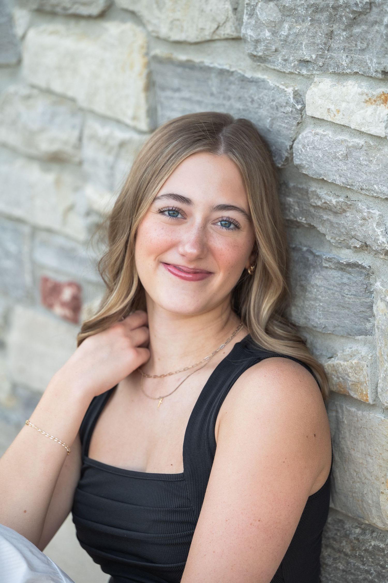 A series of five portrait photos showing someone in a black sleeveless top posing against a textured stone wall.