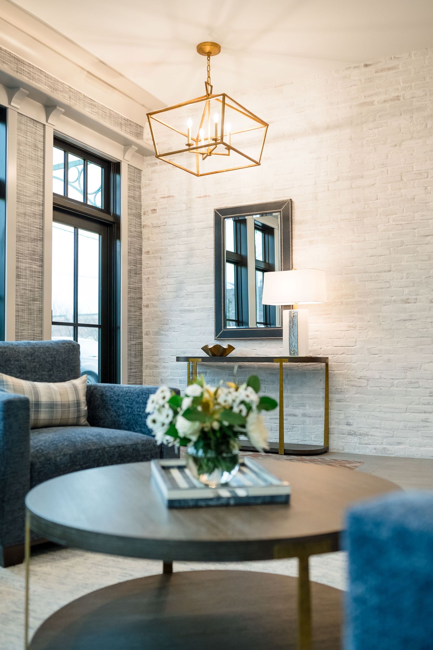 Modern living room interior with white brick walls, navy blue furniture, and gold pendant lighting fixtures.