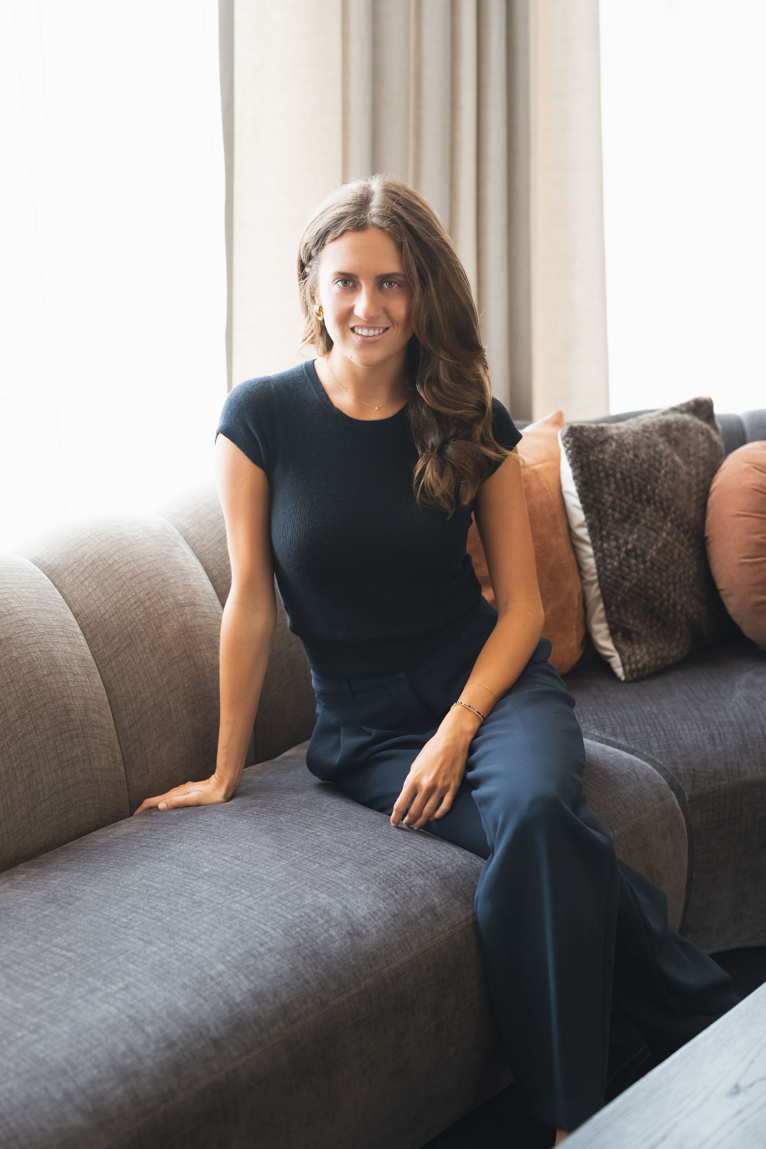 Person in navy blue outfit sits casually on a gray sectional sofa with decorative throw pillows.